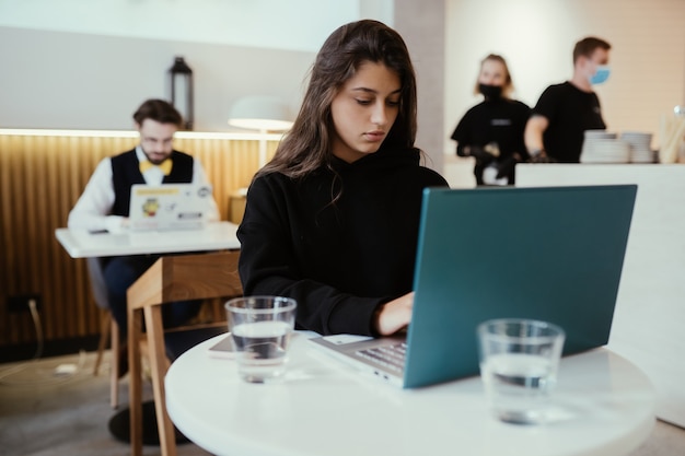 Portret van een jonge mooie vrouw werkt op draagbare laptopcomputer, charmante vrouwelijke student met behulp van net-boek zittend in café