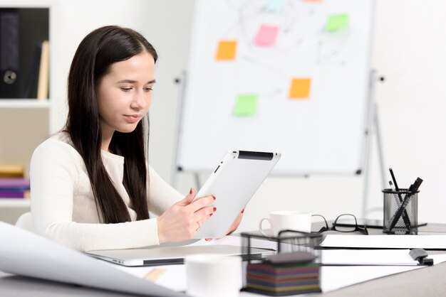 Portret van een jonge onderneemster die digitale tablet in het bureau bekijkt