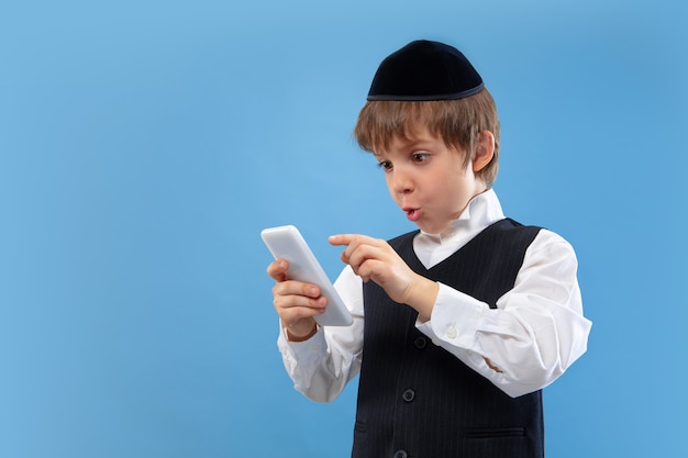 Gratis foto portret van een jonge orthodoxe joodse jongen die op blauwe muur wordt geïsoleerd die het pascha ontmoet