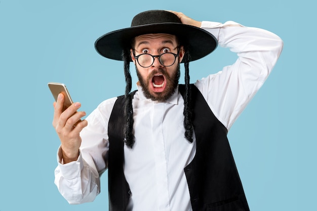 Gratis foto portret van een jonge orthodoxe joodse man met mobiele telefoon in de studio.