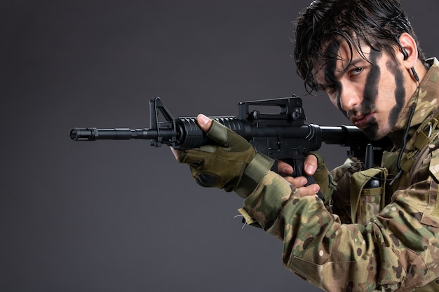 Portret van een jonge soldaat in camouflage die machinegeweer op donkere muur richt
