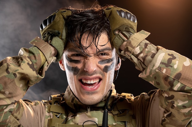 Portret van een jonge soldaat in camouflage op een donkere muur