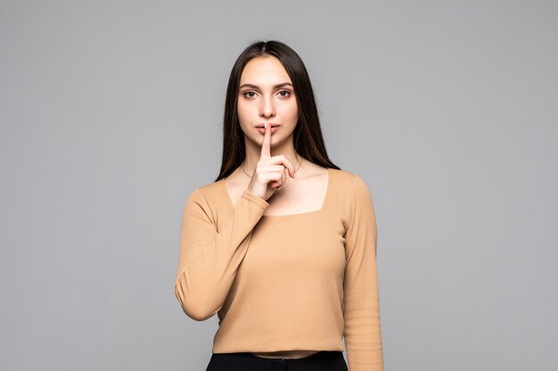 Portret van een jonge speelse vrouw die stiltegebaar toont en knipoogt geïsoleerd op de grijze muur