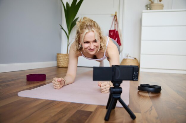 Gratis foto portret van een jonge sportieve vlogger fitness instructeur die in een plank op een rubberen yoga mat staat