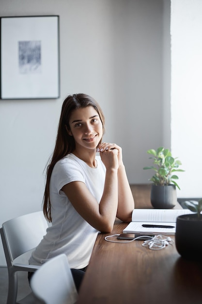 Portret van een jonge student software-ingenieur die een werkboek leest en naar de camera kijkt terwijl hij glimlacht