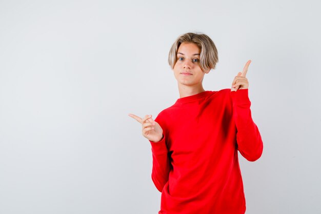 Portret van een jonge tienerjongen die naar links en rechts wijst in een rode trui en er zelfverzekerd uitziet