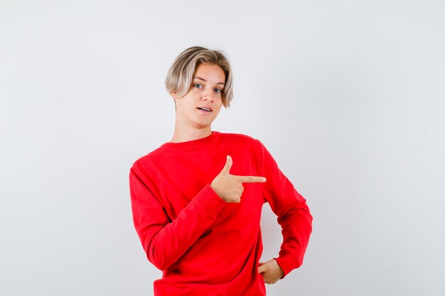 Portret van een jonge tienerjongen die naar rechts in een rode trui wijst en zelfverzekerd vooraanzicht kijkt