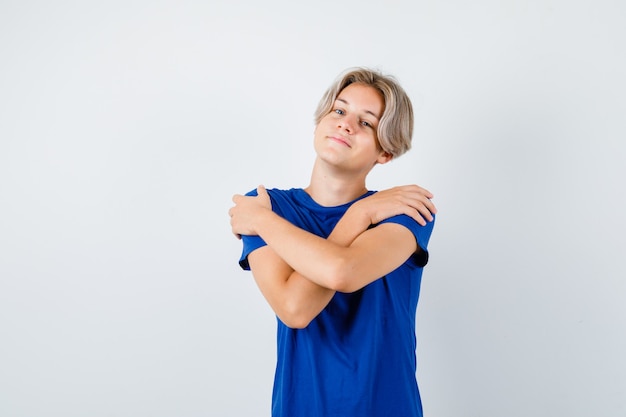 Gratis foto portret van een jonge tienerjongen die zichzelf omhelst in een blauw t-shirt en er trots uitziet vooraanzicht