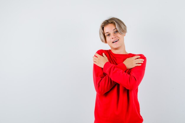 Portret van een jonge tienerjongen die zichzelf omhelst in het vooraanzicht van de rode trui