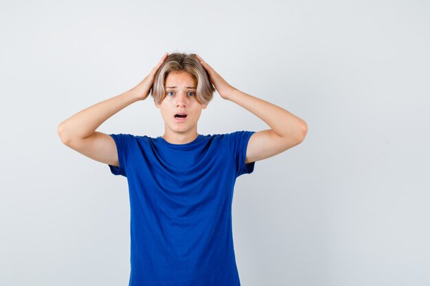 Portret van een jonge tienerjongen met de handen op het hoofd in een blauw t-shirt en een verontrust vooraanzicht