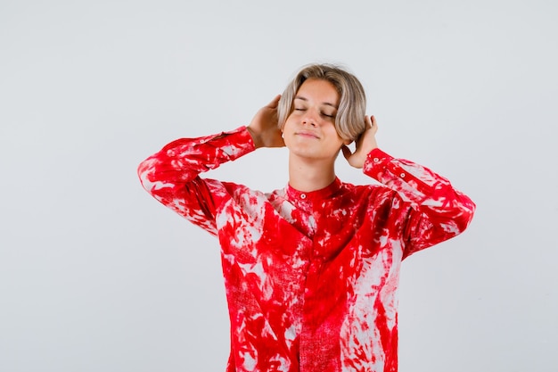 Portret van een jonge tienerjongen met handen achter de oren, ogen dicht in shirt en opgetogen vooraanzicht