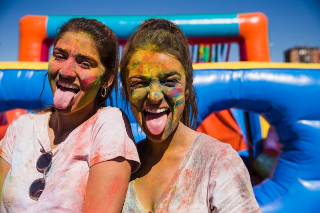 Portret van een jonge vrouw bedekt met holi gezicht steekt tong camera kijken