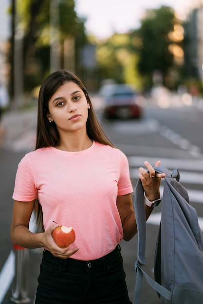 Gratis foto portret van een jonge vrouw die appel vasthoudt tegen een straatachtergrond