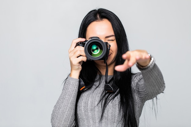 Portret van een jonge vrouw die beelden op de camera neemt, dat op grijze muur wordt geïsoleerd