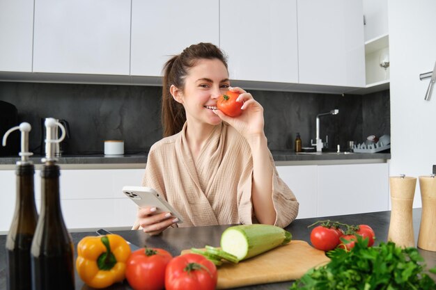 Portret van een jonge vrouw die boodschappen bestelt op de smartphone-app met tomaat die in de buurt van hakken zit