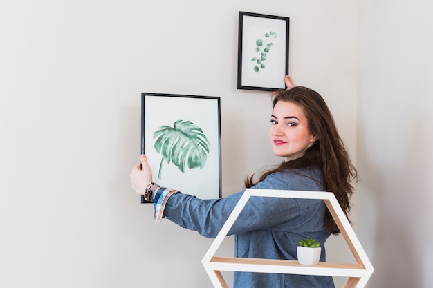 Gratis foto portret van een jonge vrouw die de omlijsting op muur bevestigt die aan camera kijkt