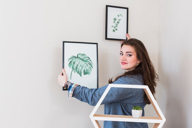 Portret van een jonge vrouw die de omlijsting op muur bevestigt die aan camera kijkt