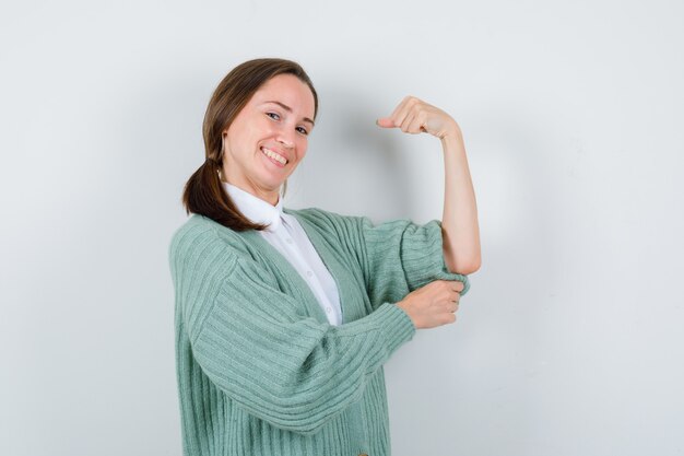 Portret van een jonge vrouw die de spieren van de arm in blouse, vest toont en er vrolijk vooraanzicht uitziet