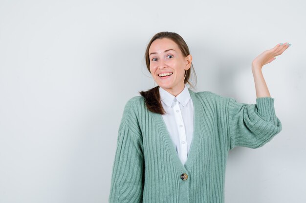 Portret van een jonge vrouw die doet alsof ze iets in een blouse, vest en een vrolijk vooraanzicht laat zien