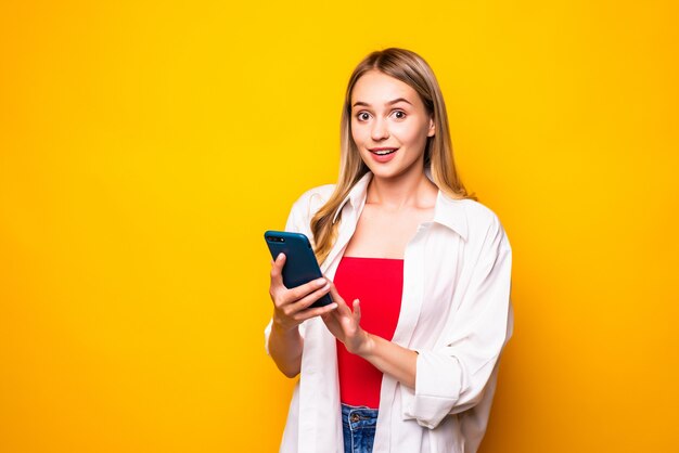 Portret van een jonge vrouw die door mobiele telefoon babbelt die over gele muurmuur wordt geïsoleerd.