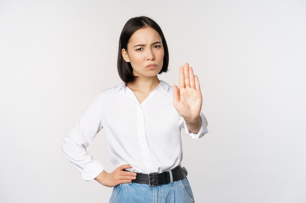 Portret van een jonge vrouw die één hand uitsteekt, stop taboe-teken dat iets afwijst dat op een witte achtergrond staat