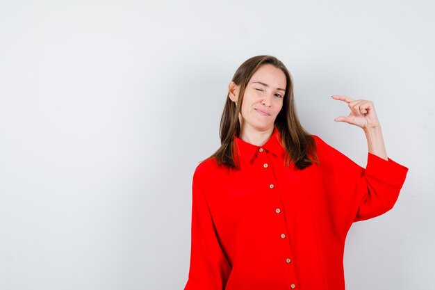 Portret van een jonge vrouw die een klein bordje laat zien terwijl ze in een rode blouse knippert en peinzend vooraanzicht kijkt