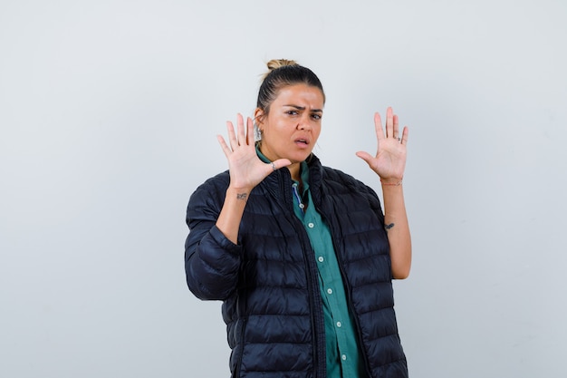 Portret van een jonge vrouw die een overgavegebaar toont in een overhemd, een pufferjack en een bang vooraanzicht