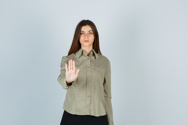 Portret van een jonge vrouw die een stopgebaar in shirt, rok toont en er serieus vooraanzicht uitziet