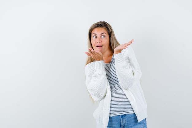 Portret van een jonge vrouw die iets in t-shirt, jasje toont en verbaasd vooraanzicht kijkt