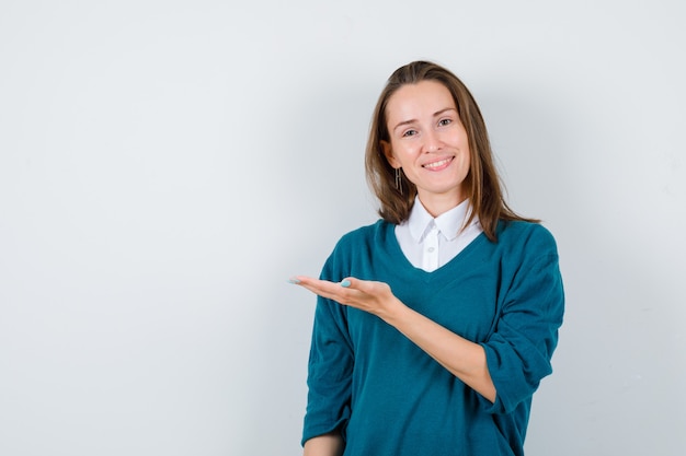 Portret van een jonge vrouw die iets op een witte muur toont of presenteert met kopieerruimte