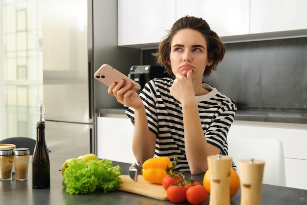 Gratis foto portret van een jonge vrouw die in de keuken staat met groenten en een snijplank vast