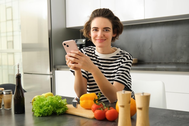Gratis foto portret van een jonge vrouw die in de keuken staat met groenten en een snijplank vast