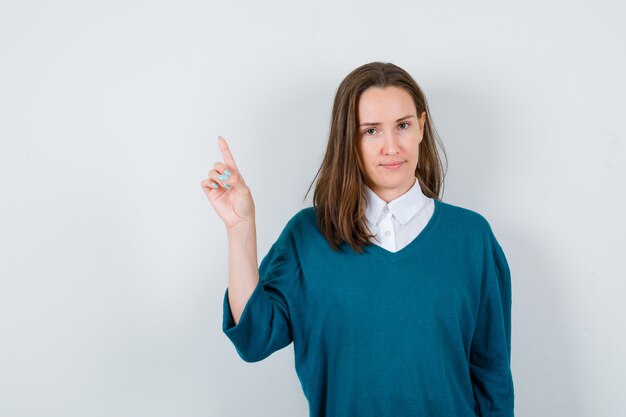 Portret van een jonge vrouw die in trui over shirt wijst en zelfverzekerd vooraanzicht kijkt