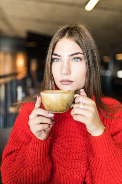 Portret van een jonge vrouw die koffie drinkt aan tafel met een notitieboekje in café