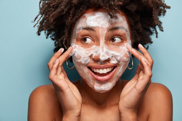 Portret van een jonge vrouw die met Afro-kapsel haar huid wast