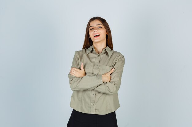 Portret van een jonge vrouw die met gekruiste armen in shirt, rok staat en er gelukkig vooraanzicht uitziet