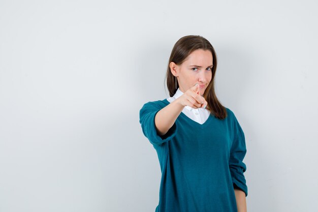 Portret van een jonge vrouw die naar voren wijst in een trui over een wit overhemd en er verstandig uitziet