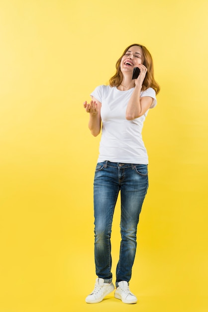 Portret van een jonge vrouw die op mobiele telefoon tegen gele achtergrond spreekt