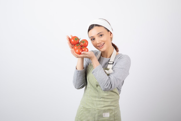 Portret van een jonge vrouw die rode tomaten over witte muur toont