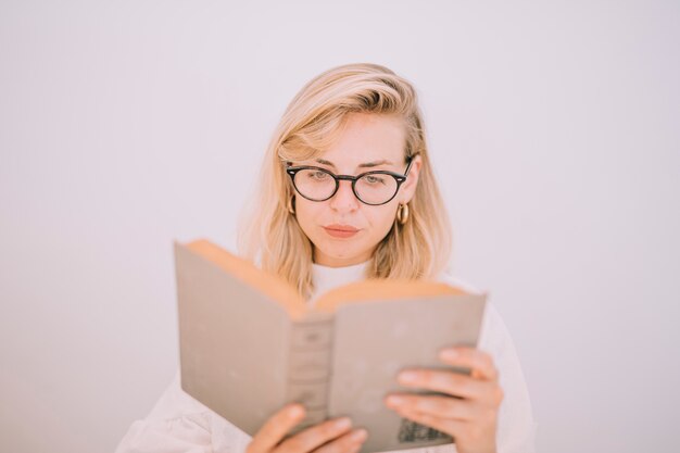 Portret van een jonge vrouw die serieus het boek leest dat op witte achtergrond wordt geïsoleerd