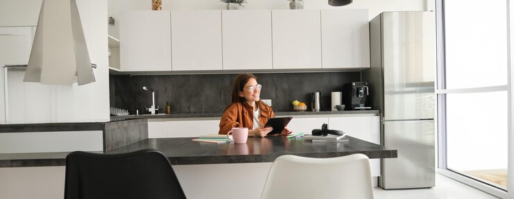 Gratis Foto portret van een jonge vrouw die thuis studeert en iets leest op een tablet die in de keuken zit