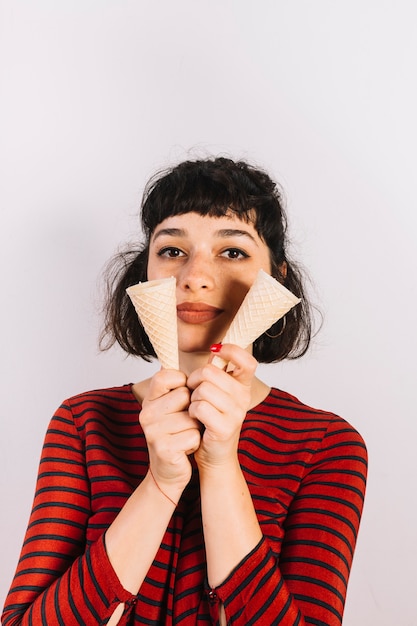 Portret van een jonge vrouw die twee lege roomijskegel op witte achtergrond toont