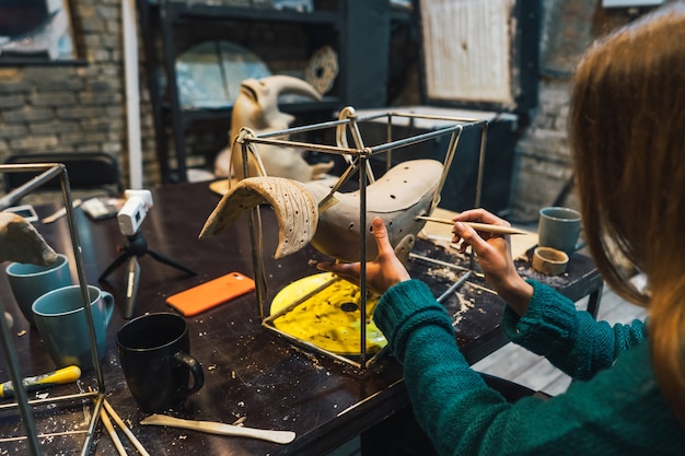 Portret van een jonge vrouw die van favoriete baan in workshop geniet. pottenbakker werkt zorgvuldig aan de kleiwalvis