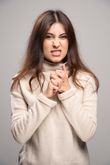 Portret van een jonge vrouw die zich voordeed op een grijze muur.