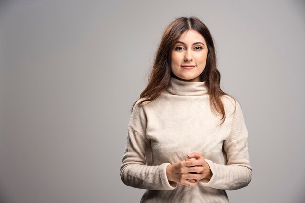 Portret van een jonge vrouw die zich voordeed op een grijze muur.