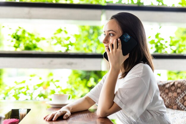 Portret van een jonge vrouw in café-restaurant die met het mobiele telefoongesprek praat en saaie gesprekken ontvangt