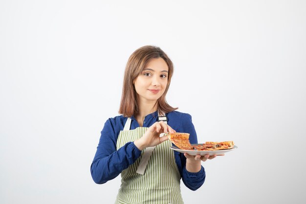 Portret van een jonge vrouw in schort die plakjes pizza op wit toont