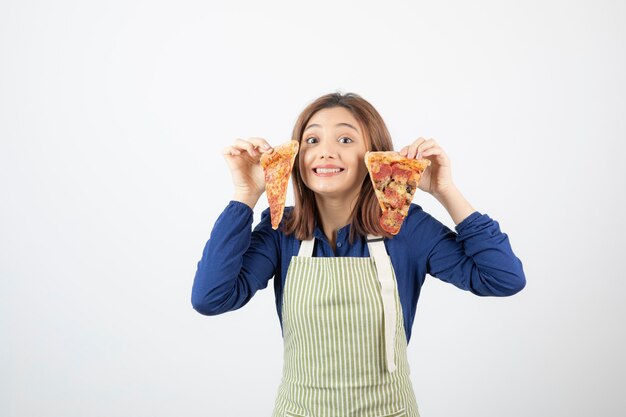 Portret van een jonge vrouw in schort die plakjes pizza op wit toont