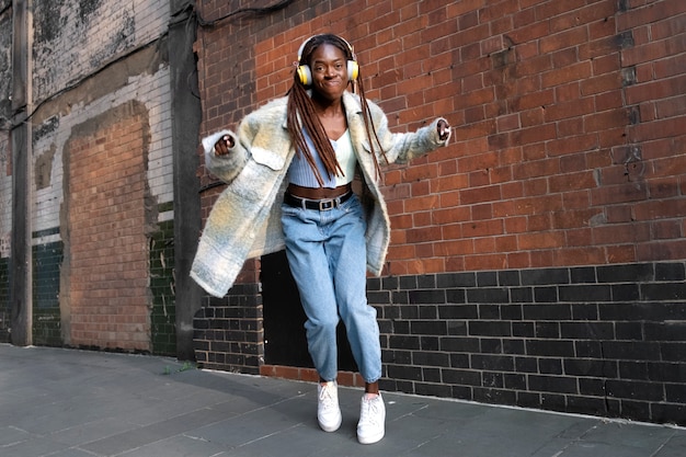 Portret van een jonge vrouw met afro-dreadlocks die dansen op muziek op een koptelefoon