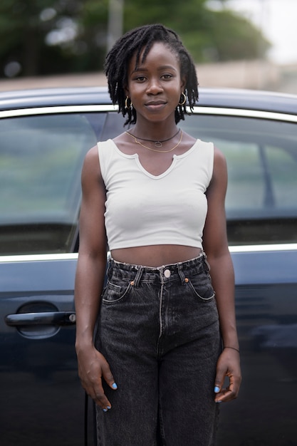 Portret van een jonge vrouw met afro-dreadlocks die naast de auto poseren